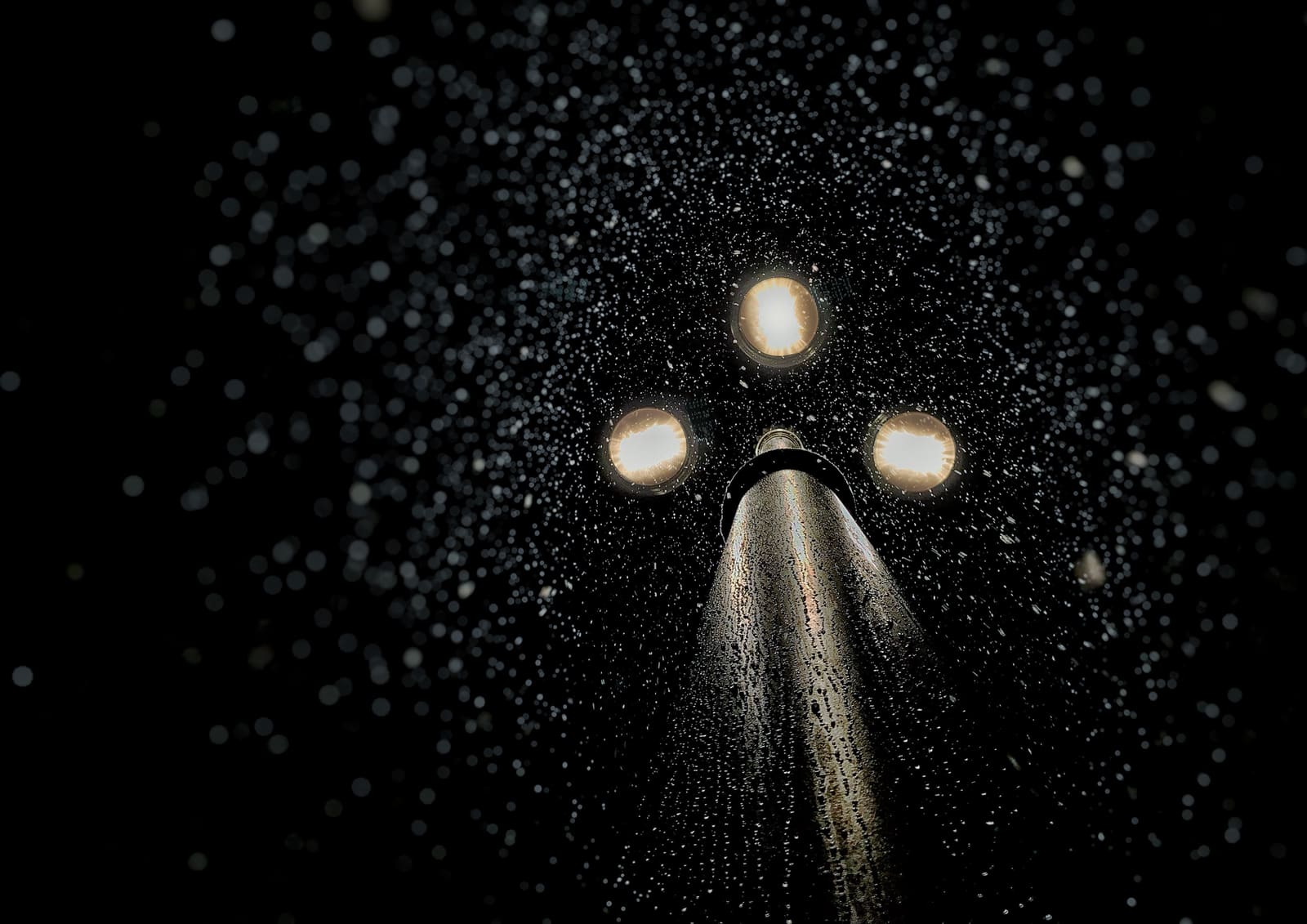 Drie brandende lampen boven op een mast in het donker, met waterdruppels in het licht